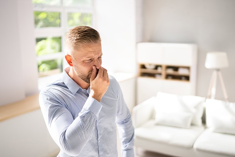 A man holding his nose as he smells somethng in his home.