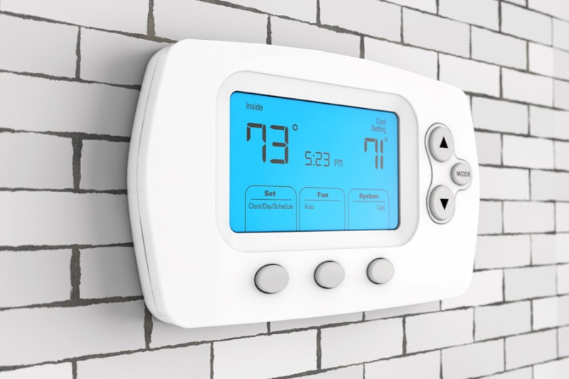 Thermostat Settings: On vs. Auto. Photo of a digital thermostat mounted on a wall with a blue light.